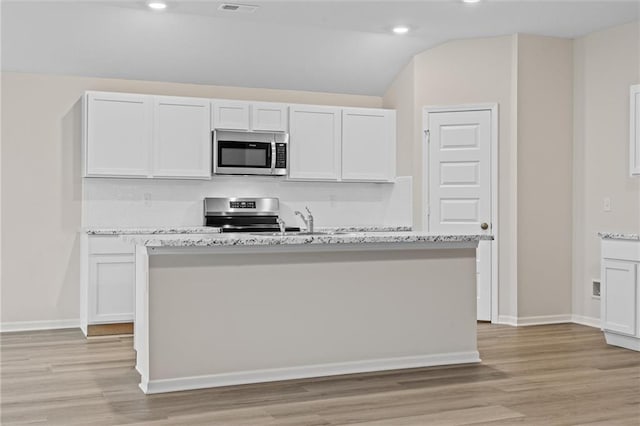 kitchen featuring lofted ceiling, stainless steel appliances, white cabinetry, light wood finished floors, and an island with sink