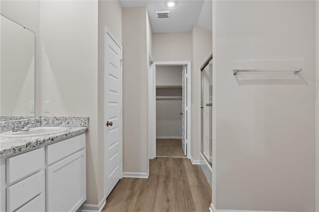 full bath with visible vents, a stall shower, vanity, wood finished floors, and baseboards