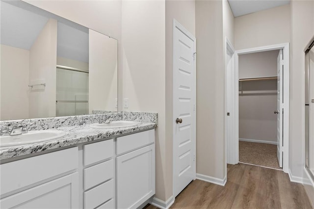 bathroom with double vanity, a stall shower, wood finished floors, a spacious closet, and a sink