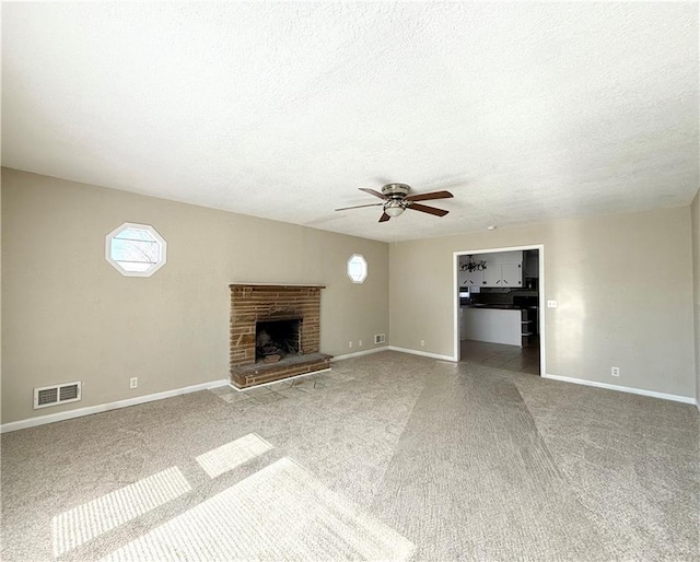 unfurnished living room with visible vents, a fireplace with raised hearth, a ceiling fan, carpet flooring, and baseboards