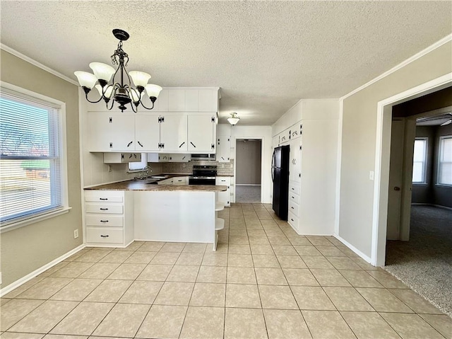 kitchen with light tile patterned floors, electric range, freestanding refrigerator, a sink, and a peninsula