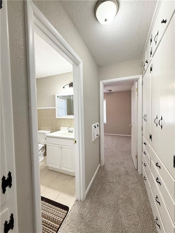 hallway featuring light carpet, baseboards, a textured wall, a textured ceiling, and a sink