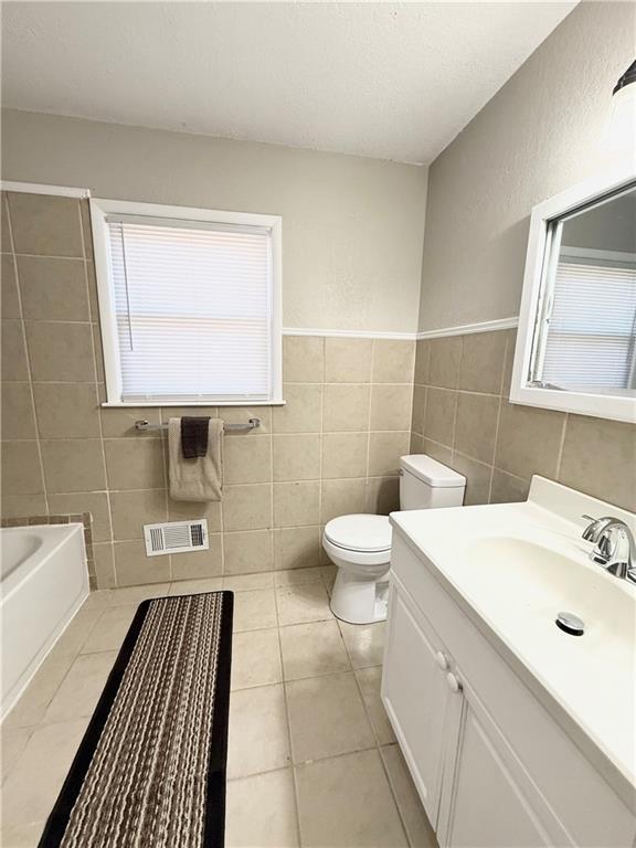 full bathroom featuring tile walls, visible vents, toilet, a tub, and tile patterned flooring