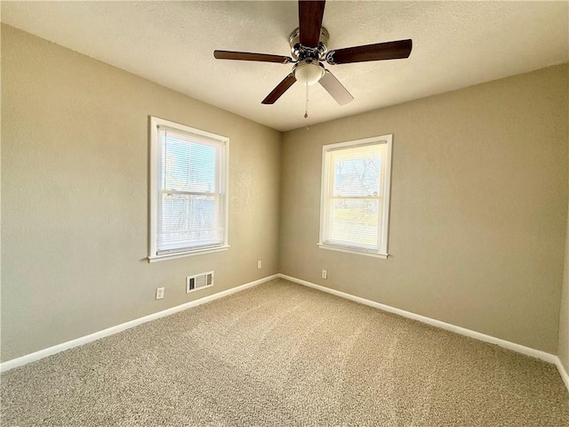 empty room with a textured ceiling, carpet, visible vents, and baseboards