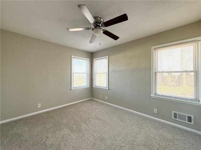 spare room featuring a wealth of natural light, baseboards, visible vents, and a textured ceiling