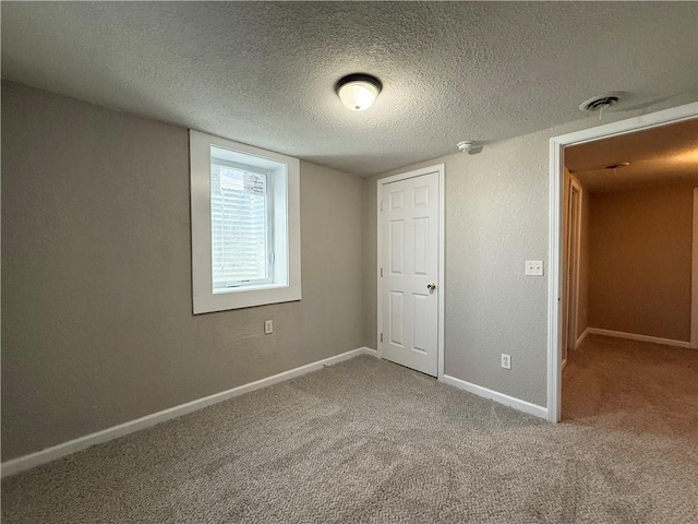 unfurnished bedroom featuring a textured ceiling, a textured wall, carpet floors, visible vents, and baseboards