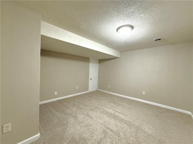 finished below grade area featuring carpet floors, baseboards, a textured ceiling, and a textured wall