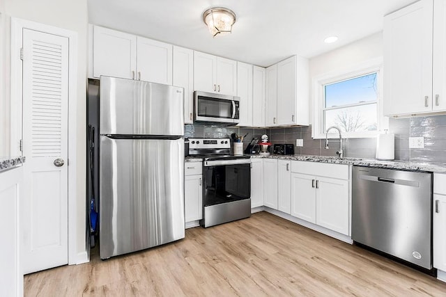 kitchen featuring stainless steel appliances, white cabinets, light wood-style flooring, and light stone counters