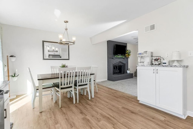 dining area featuring an inviting chandelier, light wood-style flooring, a fireplace, and visible vents