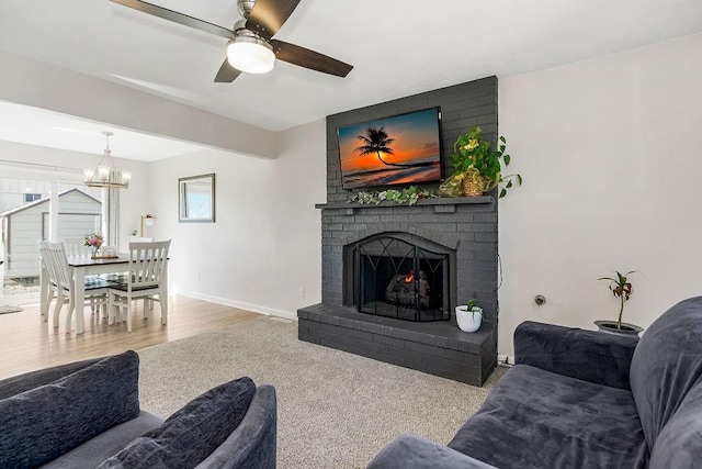 living room with a brick fireplace, baseboards, wood finished floors, and ceiling fan with notable chandelier