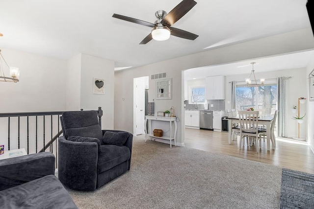 living room with light colored carpet, light wood-type flooring, visible vents, and ceiling fan with notable chandelier