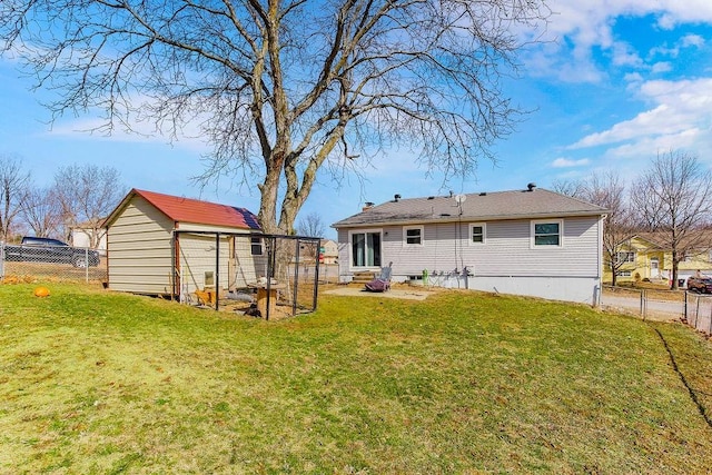 back of property featuring fence, a lawn, and an outbuilding