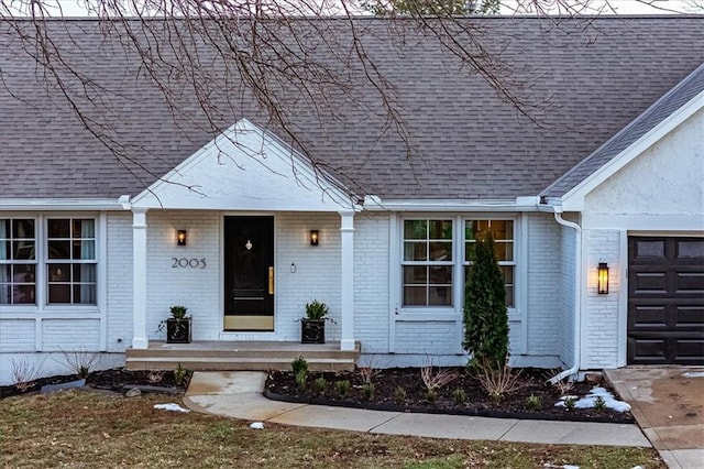 view of front of house featuring a garage, brick siding, covered porch, and roof with shingles