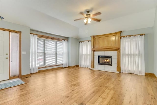 unfurnished living room with a tile fireplace, ceiling fan, light wood-style flooring, and baseboards