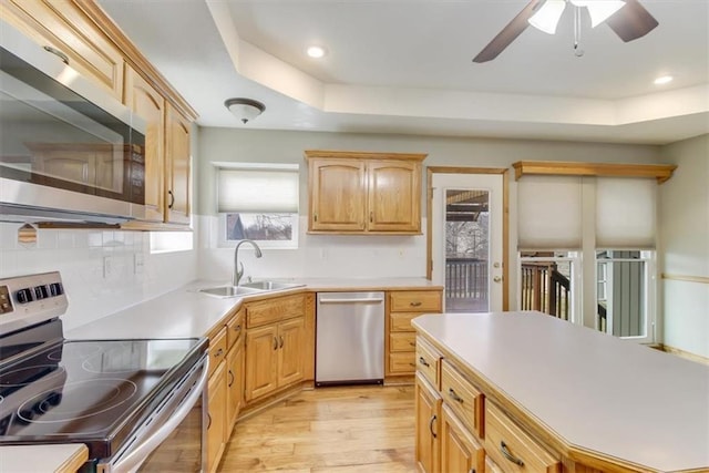 kitchen featuring stainless steel appliances, a sink, light countertops, backsplash, and light wood finished floors