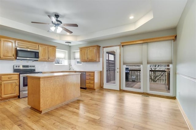 kitchen with light wood finished floors, stainless steel appliances, light countertops, and a raised ceiling