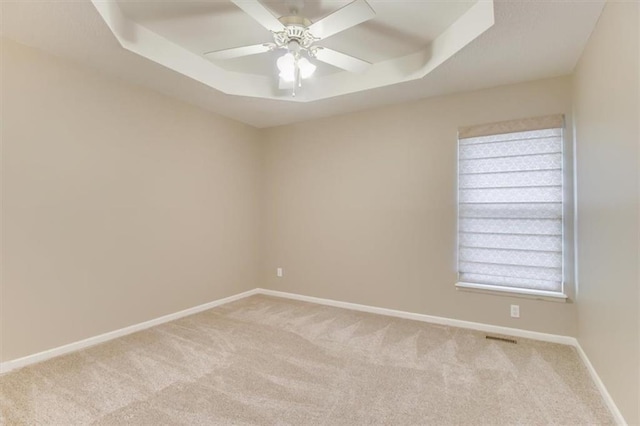 unfurnished room featuring light carpet, a tray ceiling, and baseboards