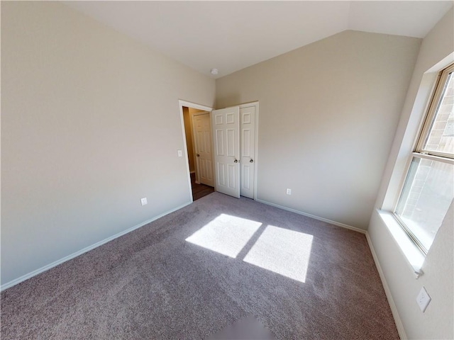 carpeted empty room featuring lofted ceiling, plenty of natural light, and baseboards