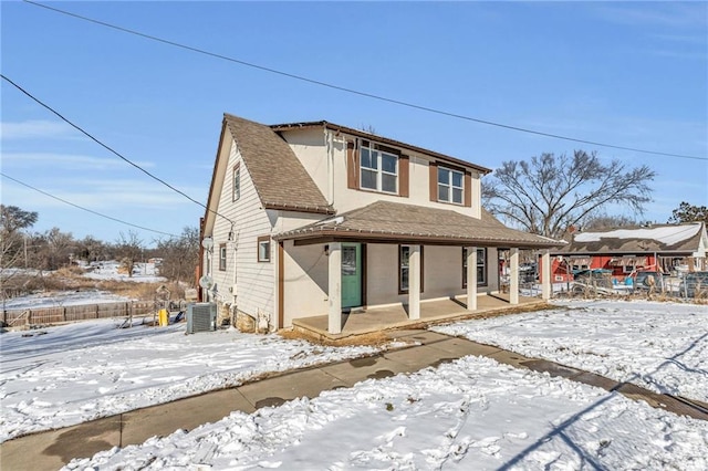 snow covered rear of property with covered porch, central AC unit, roof with shingles, and stucco siding