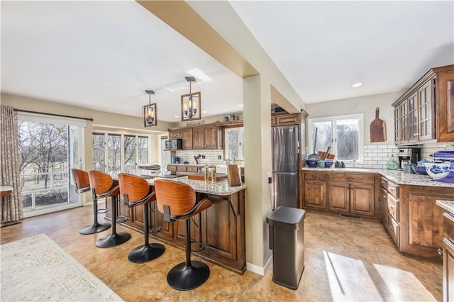 kitchen featuring a kitchen bar, glass insert cabinets, freestanding refrigerator, and light stone countertops