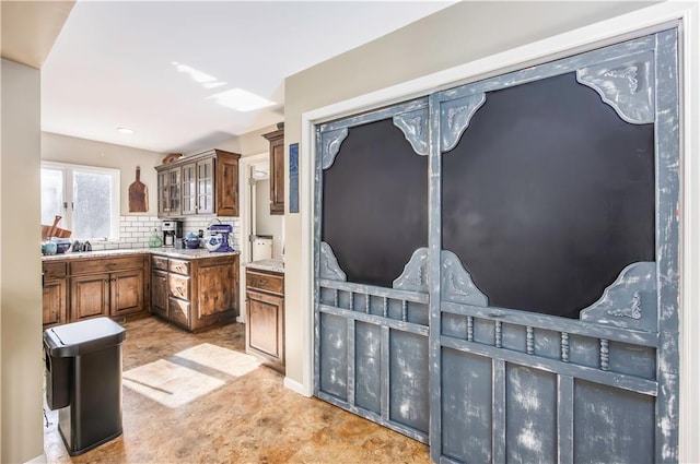 kitchen featuring decorative backsplash, glass insert cabinets, light stone counters, and brown cabinetry