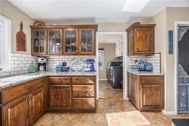 kitchen with light stone counters, backsplash, washer / clothes dryer, and glass insert cabinets