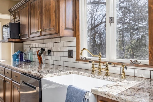 kitchen featuring a sink, light stone countertops, tasteful backsplash, and black microwave