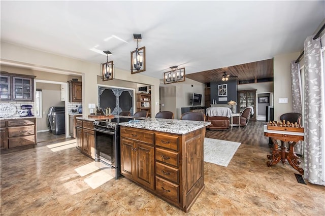 kitchen featuring glass insert cabinets, light stone countertops, open floor plan, washer / dryer, and stainless steel range with electric cooktop