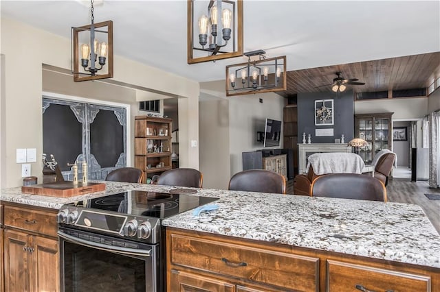 kitchen with light stone counters, open floor plan, brown cabinets, and stainless steel range with electric cooktop