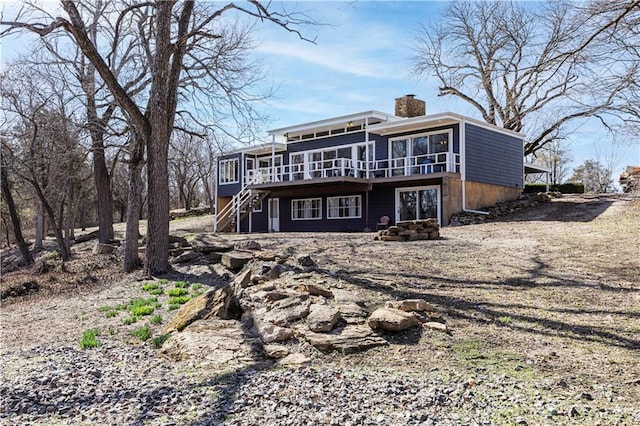 rear view of property with stairway, a chimney, a deck, and a sunroom