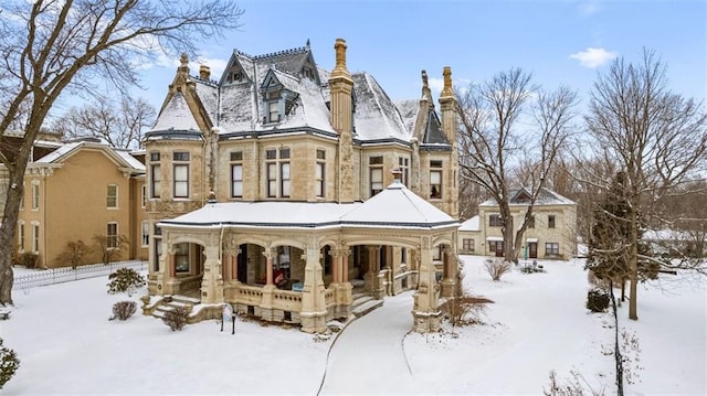 snow covered property with stone siding, covered porch, and a chimney