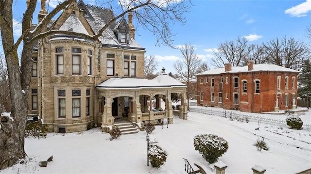 snow covered property with stone siding and covered porch