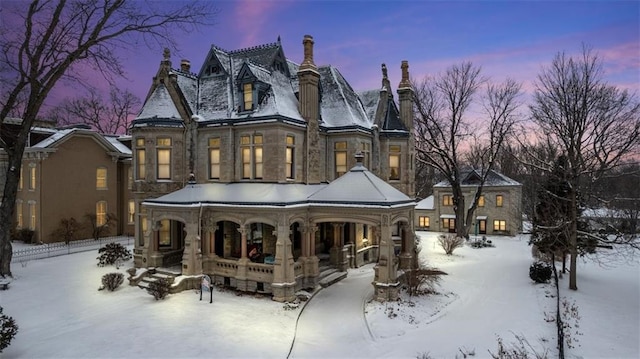 snow covered back of property featuring a porch, stone siding, and a chimney