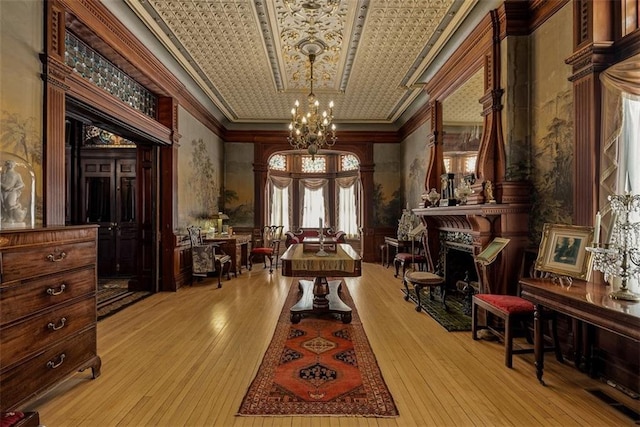 living area featuring a notable chandelier, a fireplace, ornamental molding, wood-type flooring, and an ornate ceiling