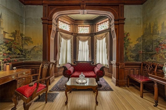 living area with wainscoting, decorative columns, a decorative wall, and light wood finished floors