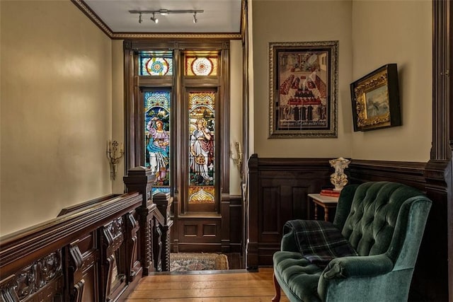 sitting room featuring hardwood / wood-style flooring, track lighting, crown molding, and wainscoting