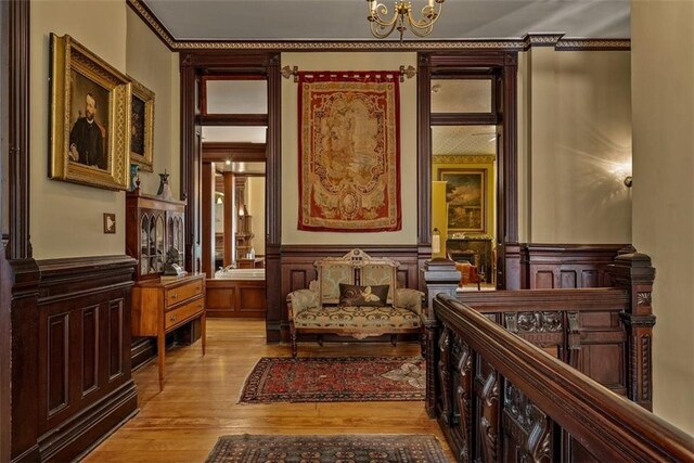 sitting room featuring a wainscoted wall, light wood-style flooring, ornamental molding, and an inviting chandelier