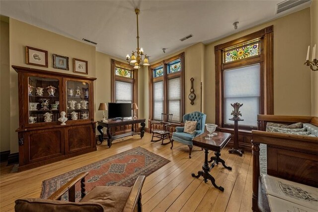 living area with light wood-type flooring, visible vents, and a notable chandelier