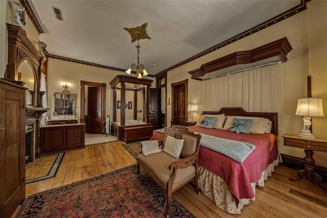 bedroom featuring a chandelier, a fireplace, visible vents, light wood-style floors, and ornamental molding