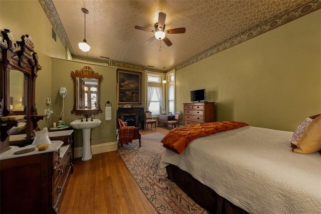 bedroom featuring a fireplace, a sink, a textured ceiling, wood finished floors, and baseboards