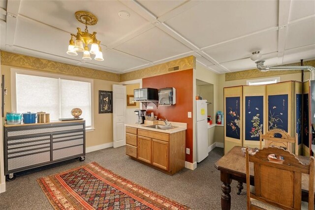 kitchen featuring brown cabinets, light countertops, freestanding refrigerator, a sink, and baseboards