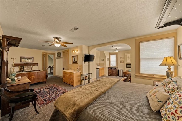 bedroom featuring visible vents, arched walkways, connected bathroom, ceiling fan, and dark colored carpet