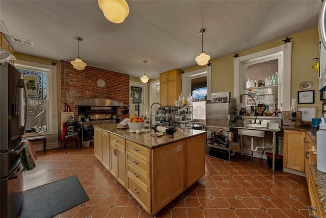 kitchen with a brick fireplace, visible vents, stainless steel refrigerator with ice dispenser, and decorative light fixtures