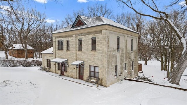 snow covered property with stone siding and a detached garage