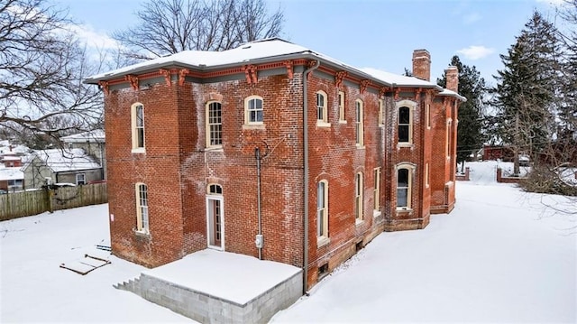 view of snowy exterior featuring a chimney, fence, and brick siding