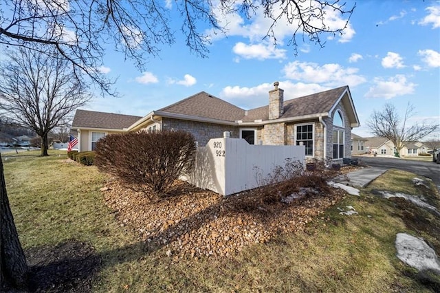 view of side of property with stone siding, a chimney, roof with shingles, fence, and a yard