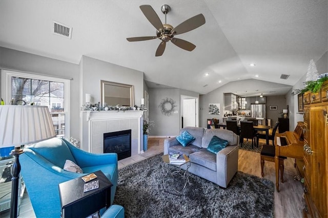 living room with visible vents, a ceiling fan, a tile fireplace, lofted ceiling, and wood finished floors