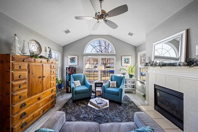 interior space featuring visible vents, a ceiling fan, a tile fireplace, lofted ceiling, and a textured ceiling