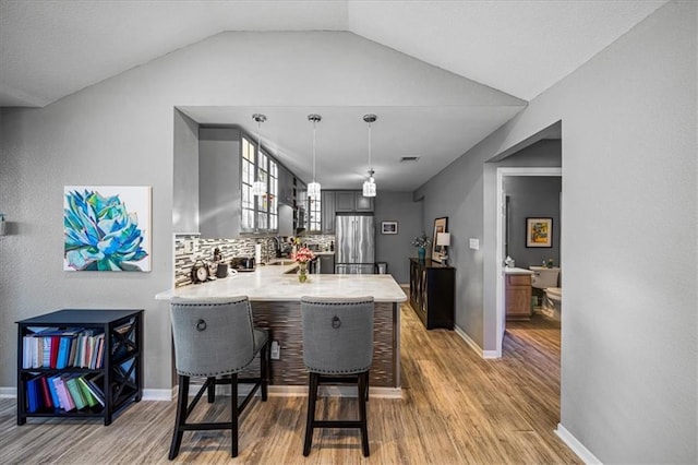 kitchen featuring light wood finished floors, light countertops, decorative backsplash, freestanding refrigerator, and a peninsula