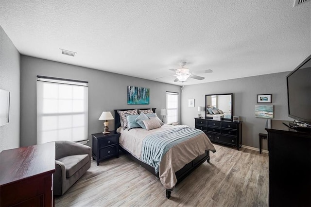 bedroom with a textured ceiling, ceiling fan, light wood-type flooring, and visible vents